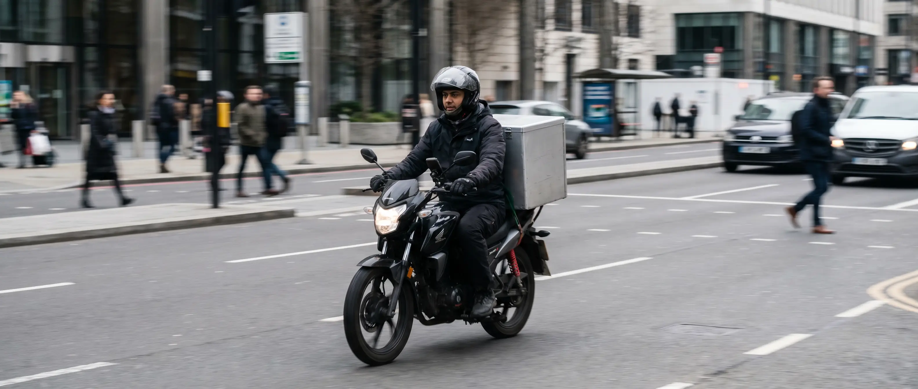 Courier on a motorbike delivering a parcel through a city street